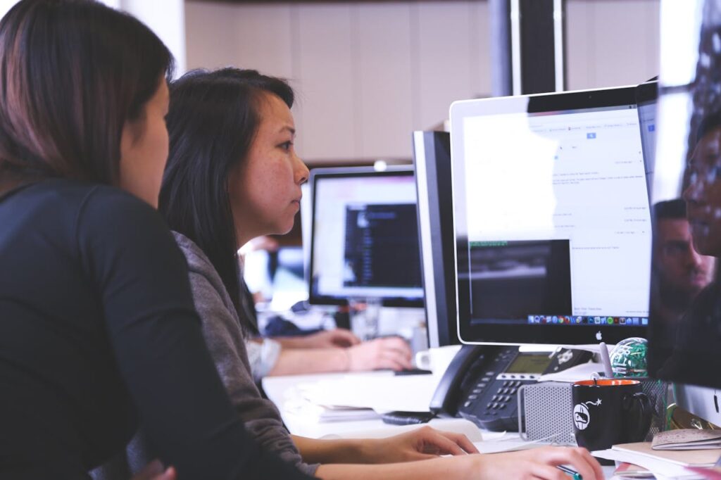 Two women working together on code at a computer in a modern office setting.